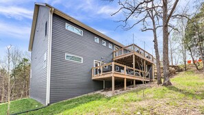 Une maison moderne à deux étages, dotée d’une terrasse en bois et d’une grande fenêtre.
