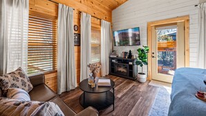 A cozy room with a sofa, a round coffee table, a TV, and a door leading outside. - Smoky Mountain Cabin: Hot Tub, BBQ & Fire Pit (Sevierville)