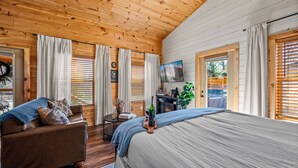 A wooden cabin interior with a bed, a sofa, a TV, and a dining table. - Smoky Mountain Cabin: Hot Tub, BBQ & Fire Pit (Sevierville)