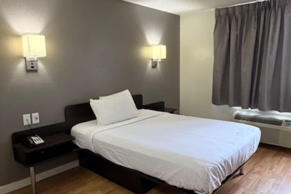 Ein Hotelzimmer mit Bett, Nachttischlampen, einem Heizgerät und einem Fenster mit Vorhängen.