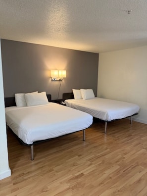 Una habitación con dos camas individuales, una lámpara fijada a la pared y suelo de madera.