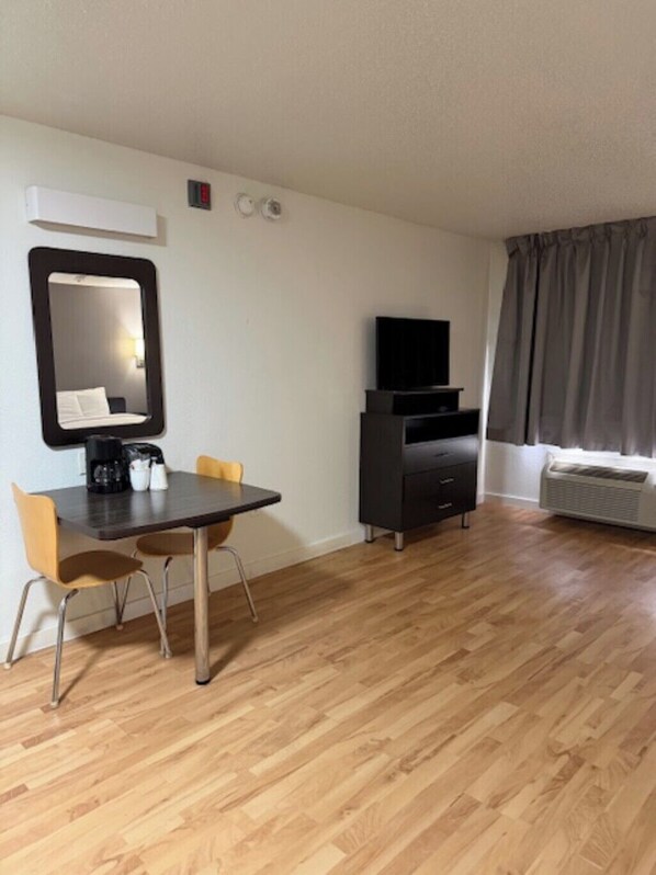 A room with a dining table, chairs, a mirror, a television, a dresser, and a window with curtains. - Suburban Studios Dallas Northwest Walnut Hill (Dallas)