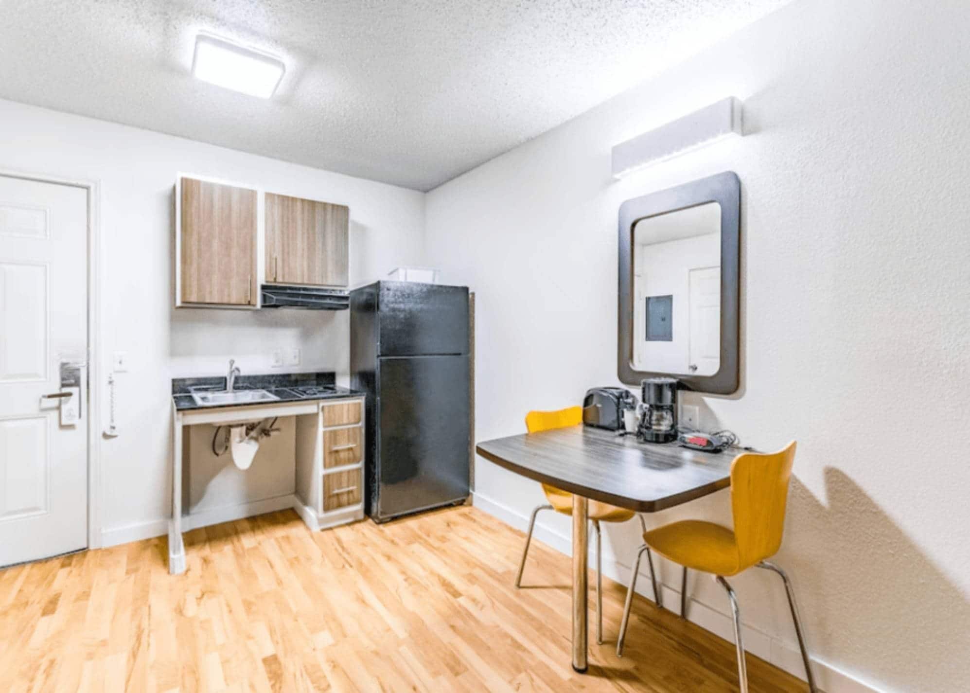 A compact kitchen with a refrigerator, a sink, and a small dining table with chairs.