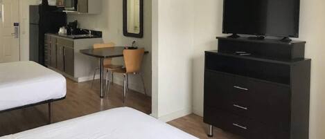 Habitación de hotel con cama, televisor en un mueble bajo, kitchenette pequeña y zona de comedor con una silla.
