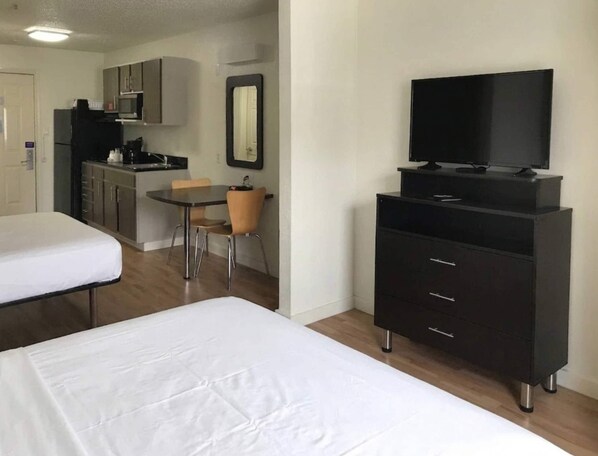A hotel room with a bed, a TV on a stand, a small kitchenette, and a dining area with a chair.
