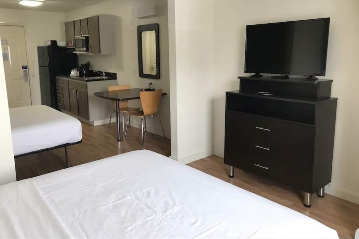 Ein Hotelzimmer mit Bett, Fernseher, Schminktisch, Stuhl und einer Küchenzeile.