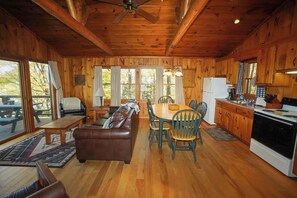 A wooden cabin interior with a dining table, chairs, a sofa, a kitchen area, and a ceiling fan. - Relaxing Lakeside Cabin on Minerva Lake-Camp 12 (Olmstedville)