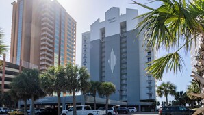 A multi-story hotel with a prominent logo, parking area, and palm trees. - Gulf Front 3rd Floor 2/2 - Large Balcony - Keyless Entry - Steps From the Beach (Gulf Shores)
