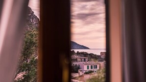 Blick auf die Küste durch ein Fenster, mit einem Berg im Hintergrund, Wasser und Gebäuden mit grünen Fensterläden.