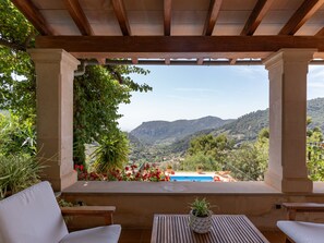 Un espace extérieur abrité, aménagé avec des sièges, offrant une vue sur un paysage montagneux et une piscine.