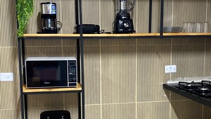 A kitchen with a microwave, coffee maker, blender, and gas stove. Shelves are used for storage. - Holiday Ranch (Japaratinga)