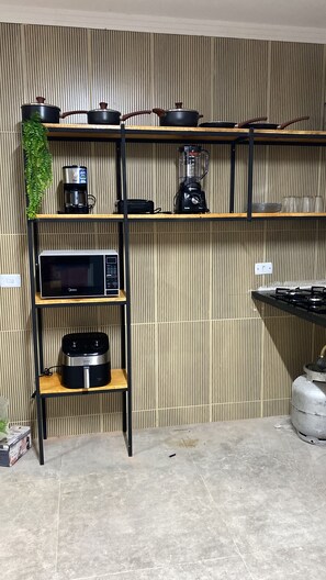 A kitchen with a microwave, coffee maker, blender, and gas stove. Shelves are used for storage. - Holiday Ranch (Japaratinga)