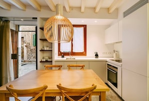 Eine moderne Küche mit Holztisch, Stühlen, einer Hängeleuchte und einem Fenster mit Fensterläden.