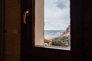 Blick durch ein Fenster mit einem Metallgriff auf eine Küstenlandschaft mit einem Gebäude und einer felsigen Küste.