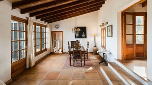 A dining area with a wooden table and chairs, a chandelier, and a view through large windows. - House "Tramuntana" - Valldemossa (Son Maxella)