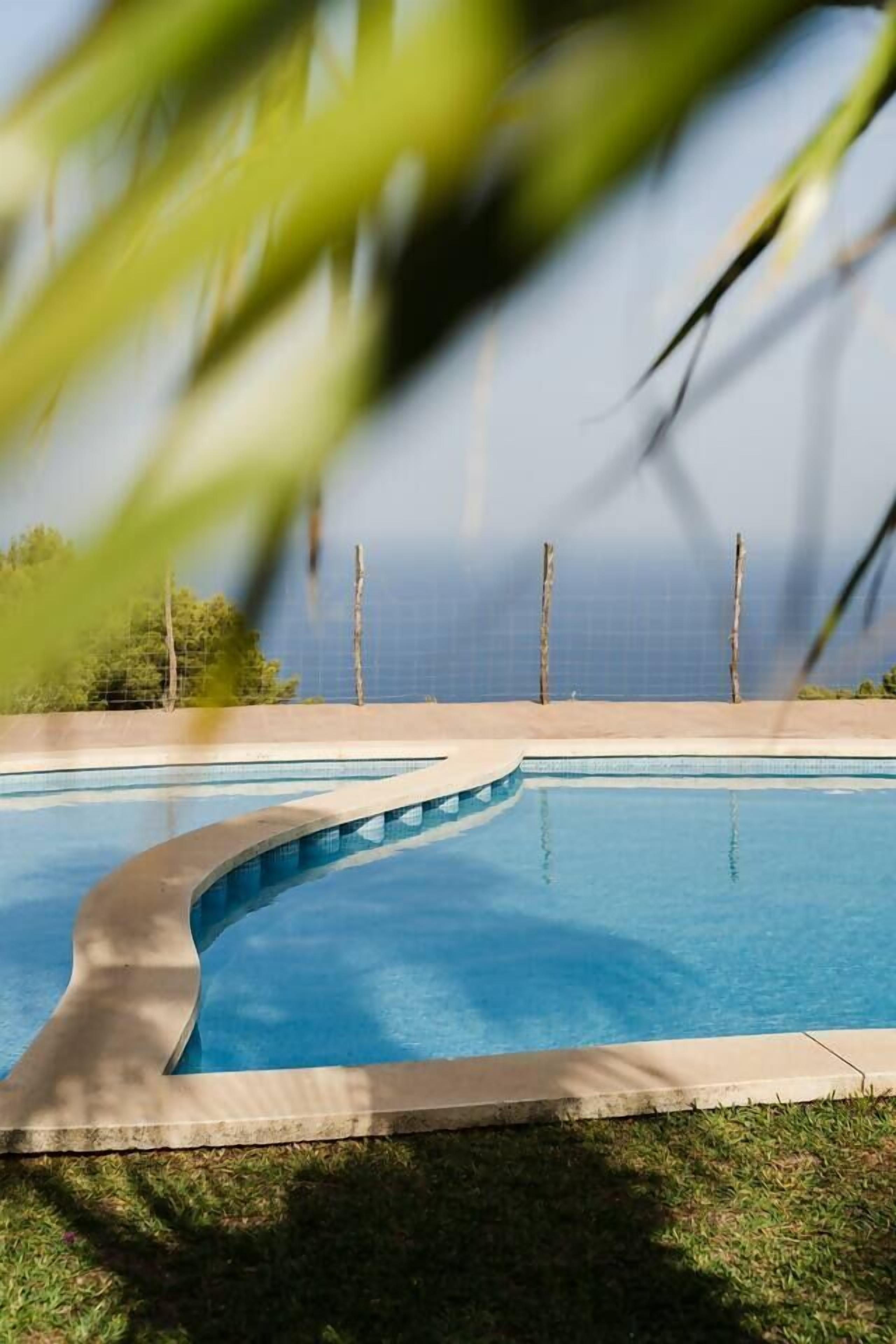 En pool med buet kant, omgivet af græs og et hegn.