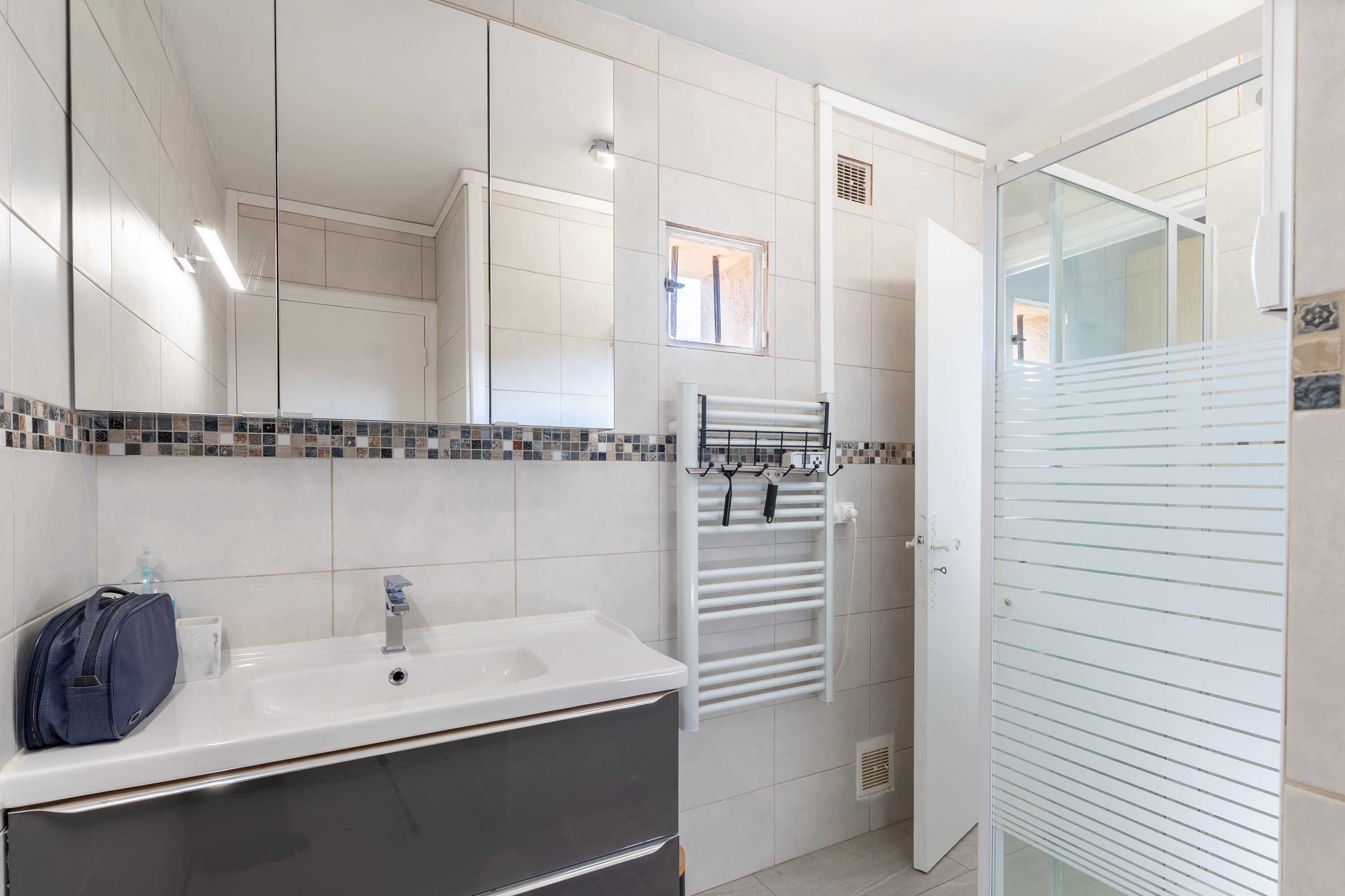 Une salle de bain avec un lavabo blanc, un porte-serviettes et une cabine de douche en verre.