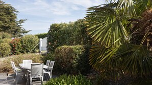 Un patio al aire libre con una mesa y sillas, rodeado de abundante vegetación y una palmera.