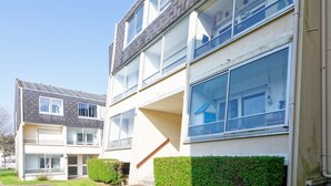 Ein mehrgeschossiges Wohngebäude mit flachem Dach, großen Fenstern und einer sichtbaren Treppe, die zu den oberen Stockwerken führt.