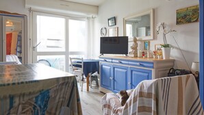 Ein Zimmer mit Fernseher, einem Esstisch, Stühlen, einem blauen Schrank und einem Fenster.