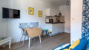 Ein gemütlicher Wohnraum mit Esstisch, Stühlen, einem Fernseher, einer Küchenzeile und einer Wand mit Muster.