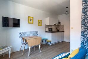 Ein gemütlicher Wohnraum mit Esstisch, Stühlen, einem Fernseher, einer Küchenzeile und einer Wand mit Muster.