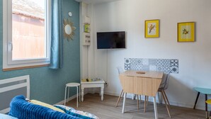 Ein Zimmer mit Bett, Tisch, Stuhl, Fernseher und einem Fenster mit Vorhängen.