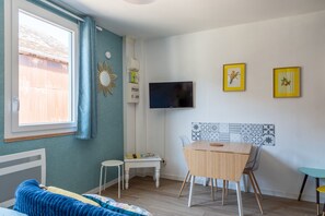 Ein Zimmer mit Bett, Tisch, Stuhl, Fernseher und einem Fenster mit Vorhängen.