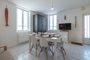 Un comedor con una mesa blanca, cuatro sillas, un televisor y un armario.