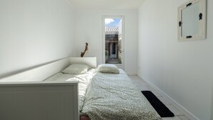 A narrow room with a bed, a door leading to an outdoor area, and a mirror on the wall. - Le Refuge Loti - 200m de la Plage (Port-des-Barques)