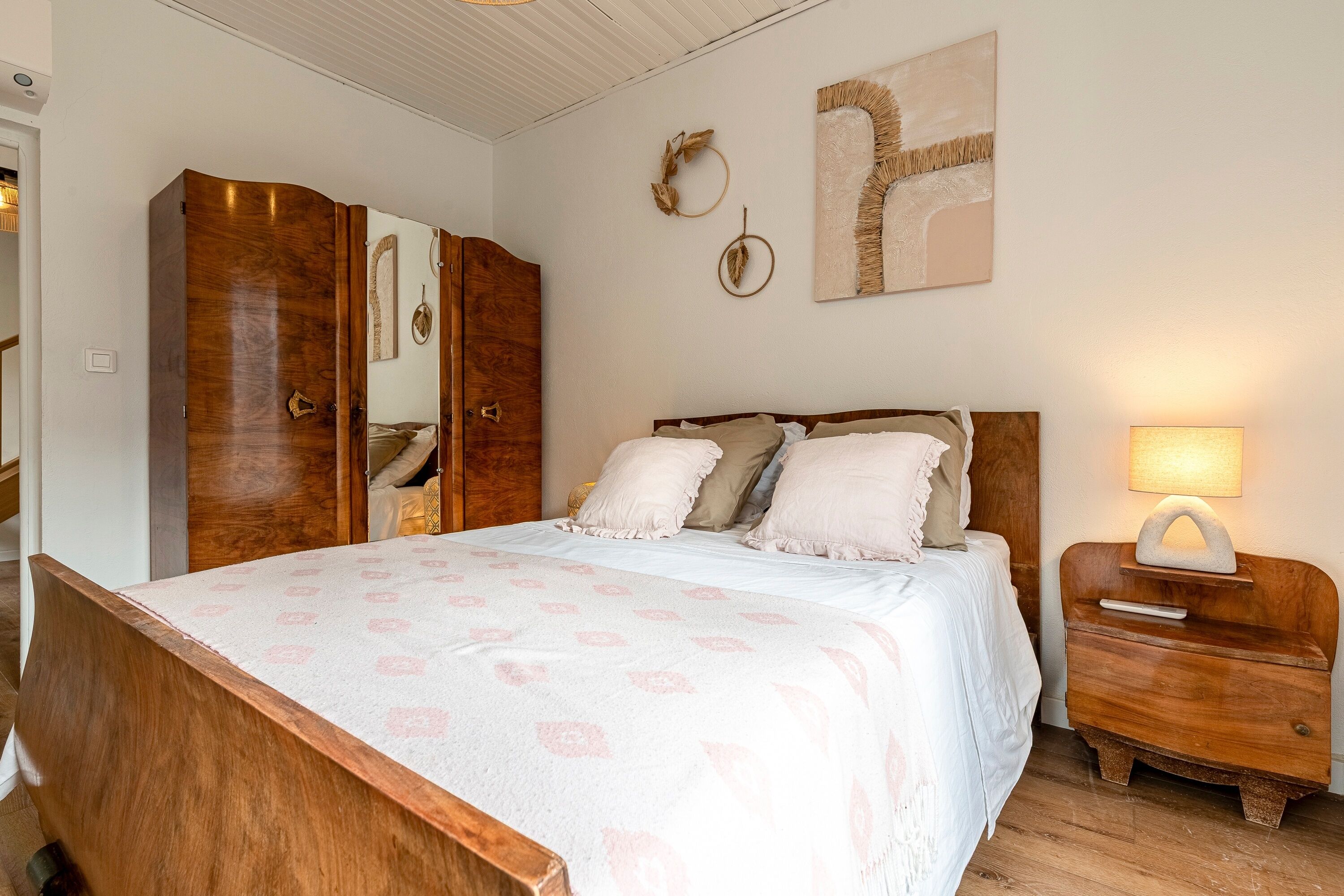 A bedroom with a wooden bed, a nightstand with a lamp, a wardrobe, and wall decorations.