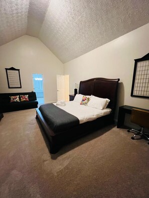 A bedroom with a bed, a chair, a couch, and a door leading to a balcony.