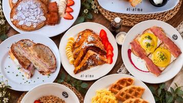 Variedad de platos de desayuno, incluyendo panqueques, huevos, gofres y tostadas, dispuestas en platos y cestas.