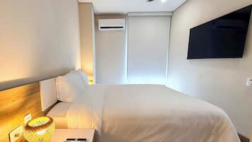 Een hotelkamer met een bed, nachtkastje, lamp en een aan de muur bevestigde televisie.