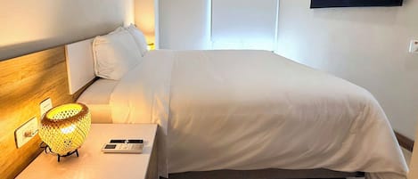 A hotel room with a bed, bedside table, lamp, and a wall-mounted TV.