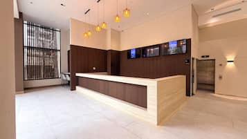 A modern reception desk with a wooden finish, multiple pendant lights, and a series of flat-screen TVs mounted on the wall.