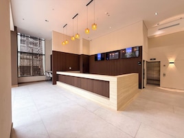 Un mostrador de recepción moderno con detalles de madera, varias luces colgantes y una serie de televisores de pantalla plana montados en la pared.