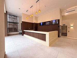 Un comptoir d’accueil moderne avec un revêtement en bois, plusieurs luminaires suspendus et une série de téléviseurs à écran plat fixés au mur.