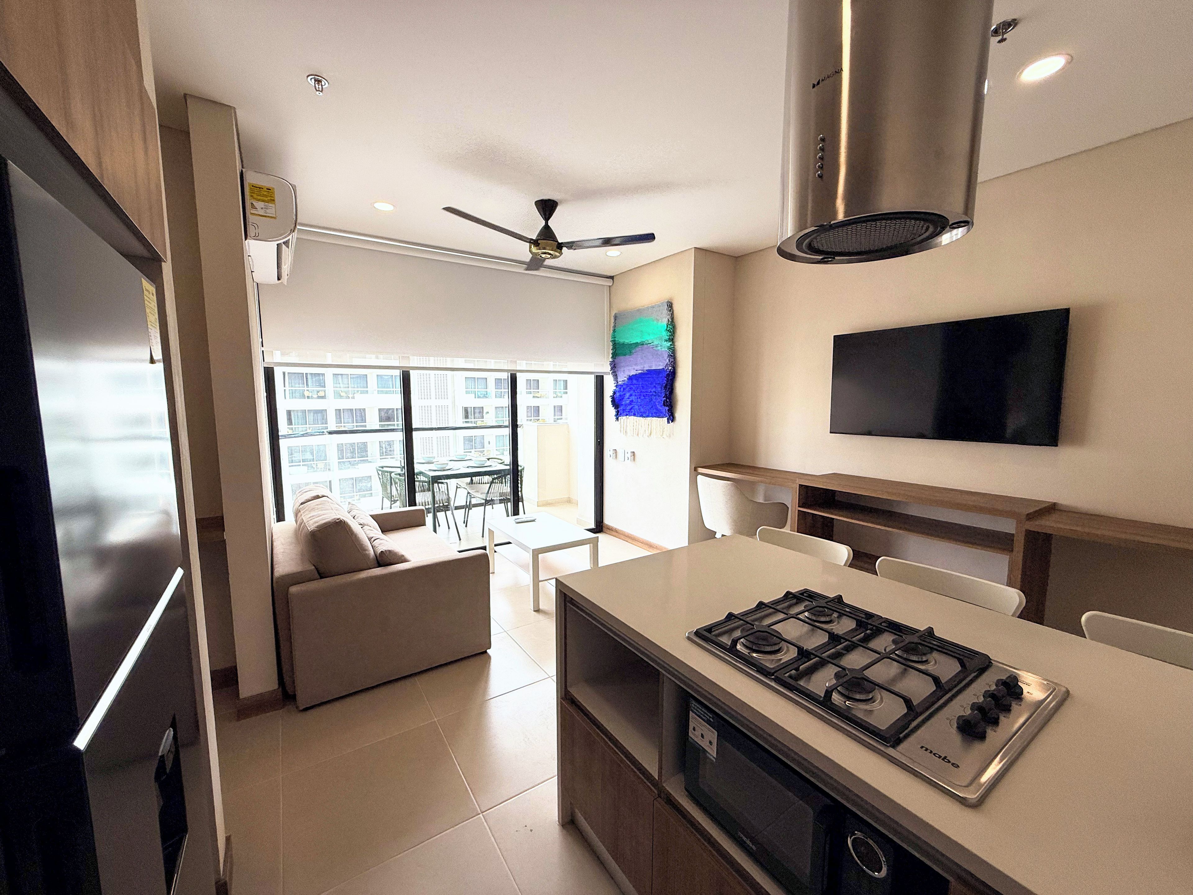 Une cuisine moderne équipée d’une cuisinière à gaz, d’un ventilateur de plafond et d’un téléviseur à écran plat fixé au mur.