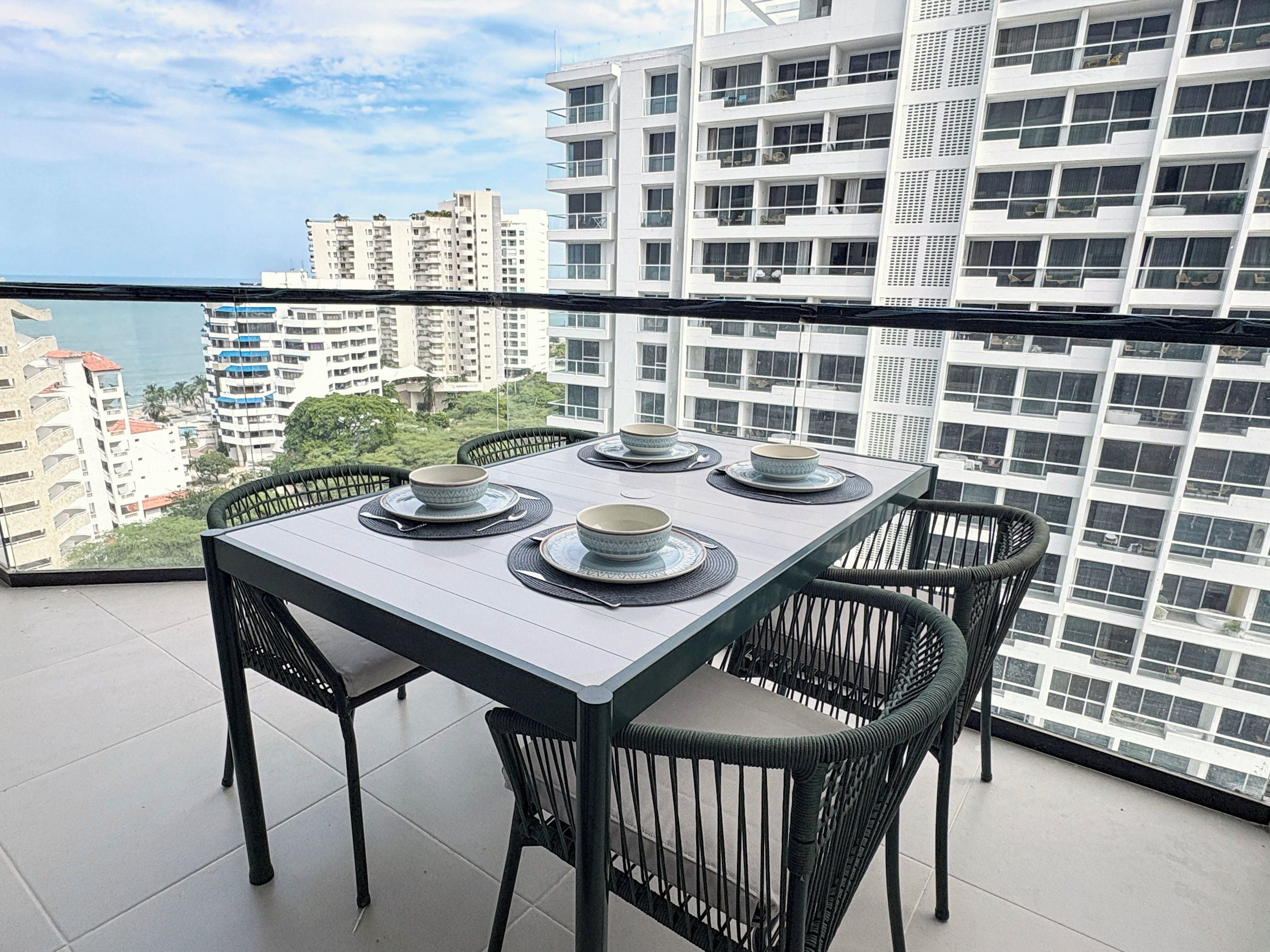 Un balcón con mesa lista para cuatro, con vistas a un paisaje urbano con edificios altos.