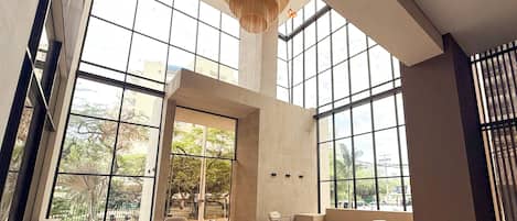 Um hall amplo com grandes janelas, mobiliário moderno e pé direito alto.