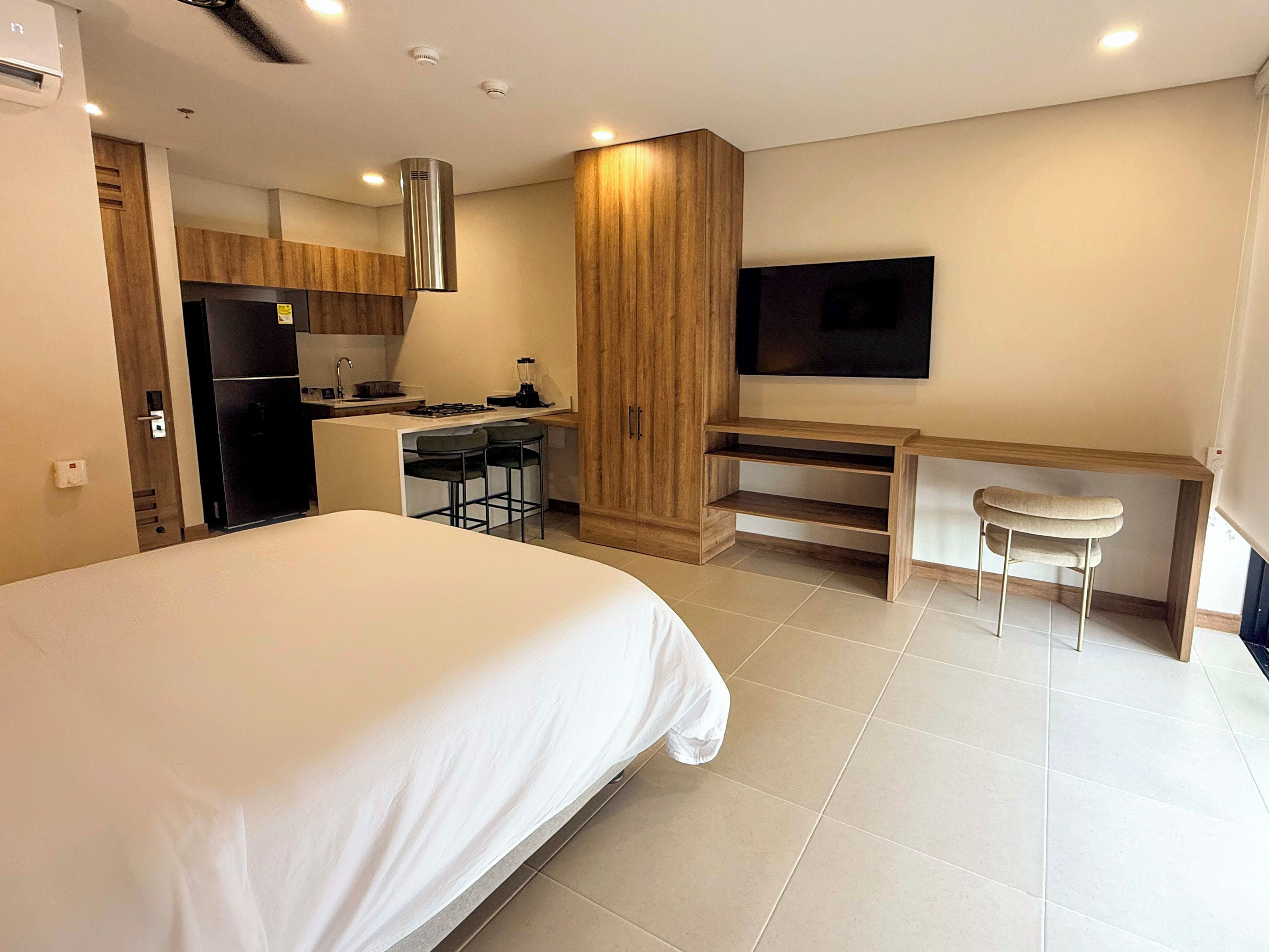 Een moderne hotelkamer met een groot bed, een kitchenette, een televisie en een bureau met een stoel.