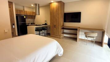 Een moderne hotelkamer met een groot bed, een kitchenette, een televisie en een bureau met een stoel.