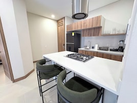 Una cocina compacta con cubierta blanca, dos sillas verdes, extractor de acero inoxidable, refrigerador negro y armarios de madera.