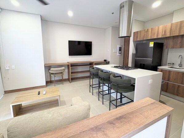 A modern kitchen with a central island, bar stools, a dining table, and a TV mounted on the wall. - Nuruma Suites by Avia Suites (Santa Marta)