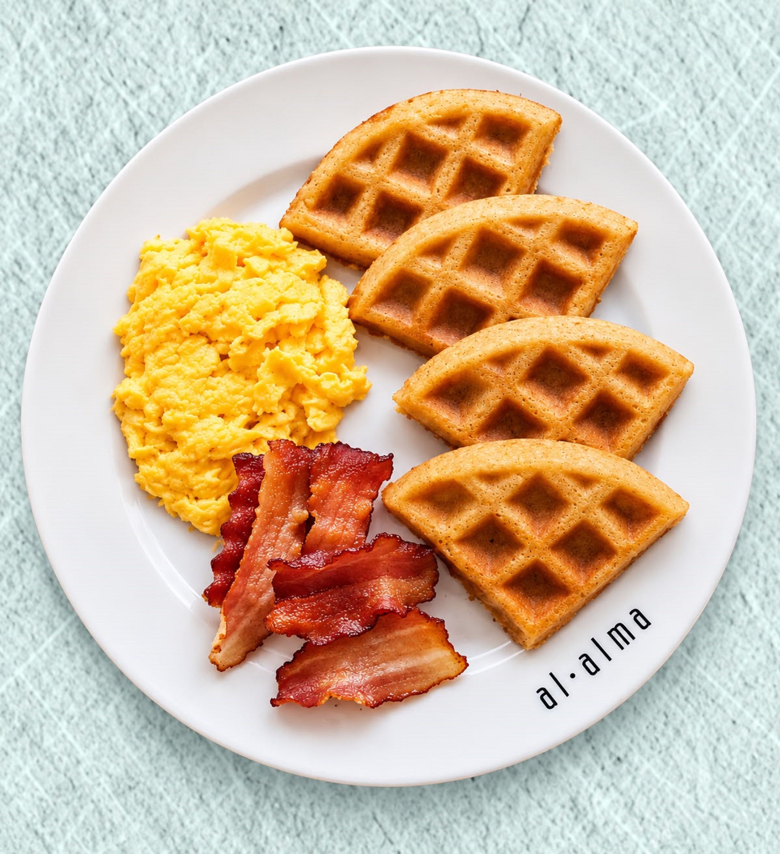 A plate with waffles, scrambled eggs, and bacon.