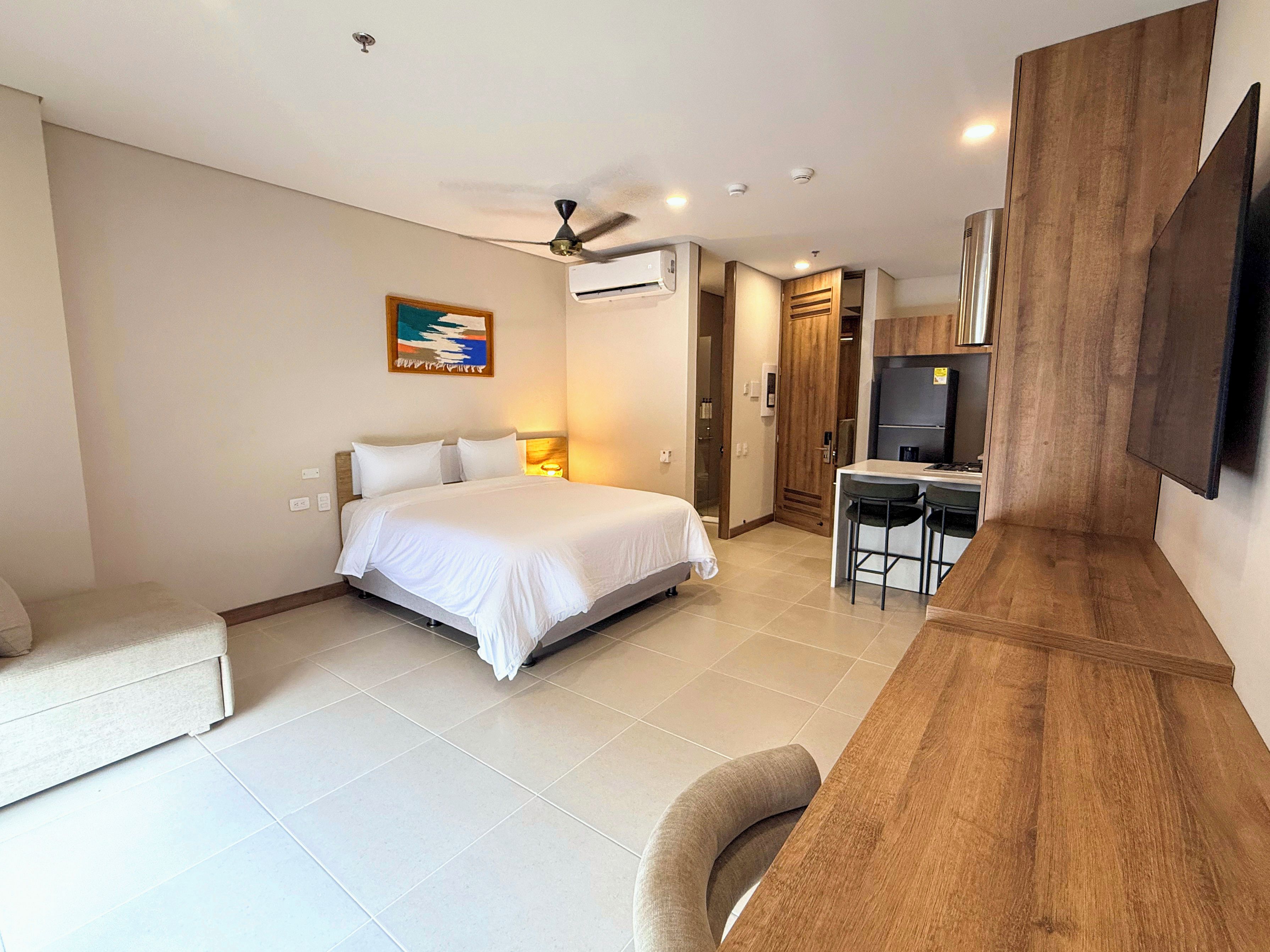 Ein Hotelzimmer mit Bett, Schreibtisch, Stuhl, Fernseher und Klimaanlage.