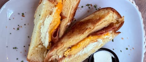 A sandwich on a white plate with a small container of butter, placed on a woven placemat.
