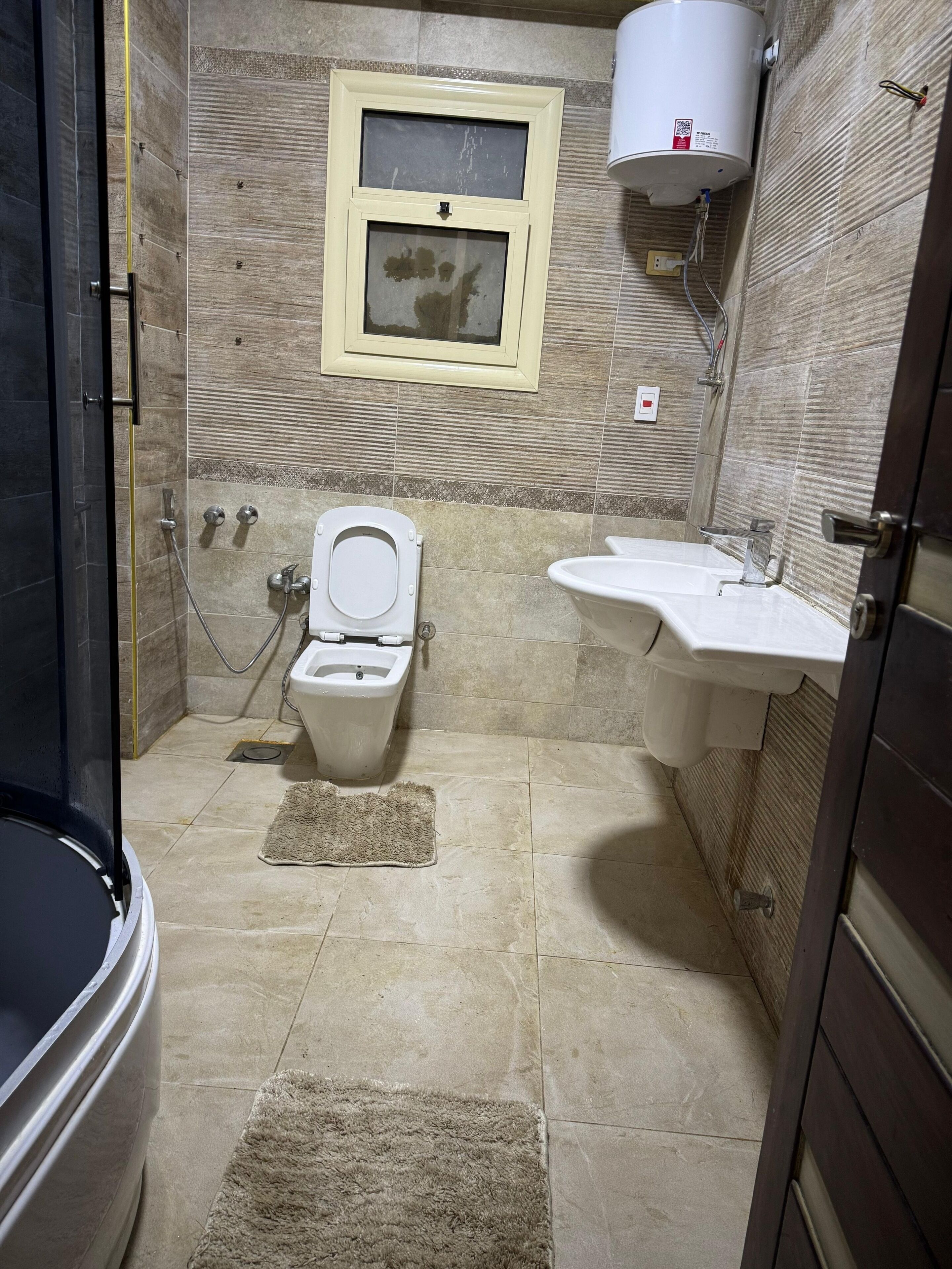A bathroom with a toilet, bidet, shower, sink, and a water heater mounted on the wall.