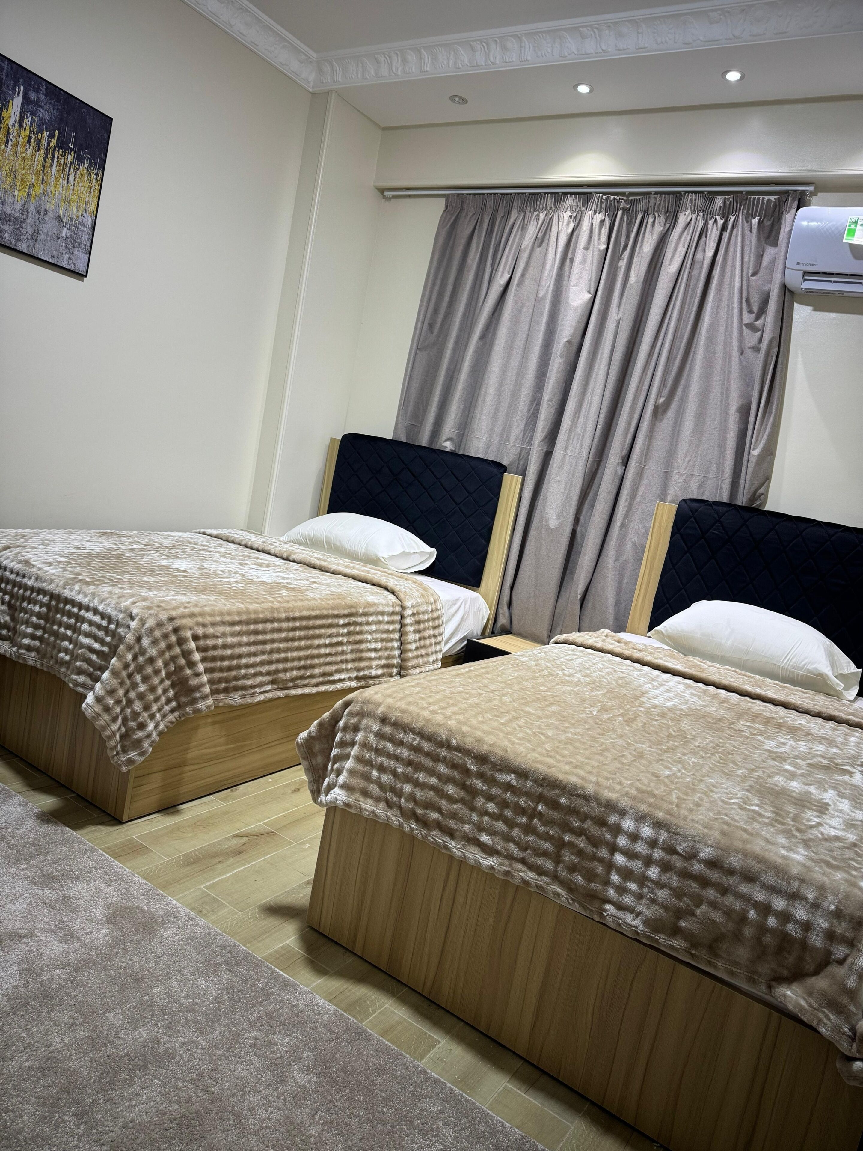Quarto de hotel com duas camas, ar condicionado no teto e janela com cortinas.